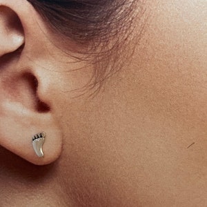 May include: Silver stud earrings in the shape of a footprint.