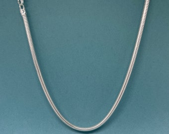 May include: A silver snake chain necklace on a blue background.