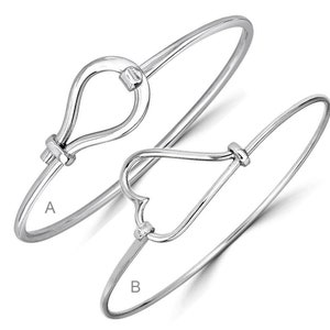 May include: Two silver bangle bracelets with different clasp designs. The bracelet labelled 'A' has a teardrop-shaped clasp, while the bracelet labelled 'B' has a heart-shaped clasp.