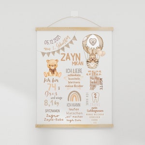 May include: A beige and brown illustrated baby milestone poster with a hot air balloon, teddy bears, and rainbows. The poster features the name "Zayn Mikan" and details about the baby's first year, including their height, weight, first words, and favorite foods.