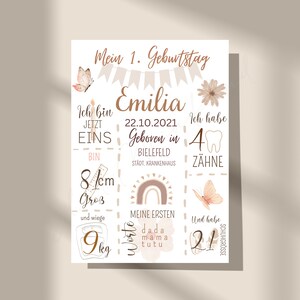 May include: A white poster with brown text and illustrations celebrating a first birthday. The poster says "Mein 1. Geburtstag" which means "My 1st Birthday" in German. The poster also says "Emilia" and includes details like the date of birth, weight, height, and first words.
