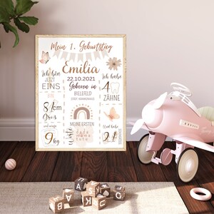 May include: A pink and white printable poster with a rainbow, butterflies, and a tooth. The poster says "Mein 1. Geburtstag Emilia 22.10.2021 Geboren in Bielefeld Stadt, Krankenhaus Ich bin jetzt eins bin 81cm gro&szlig; und wiege 9kg Ich habe 4 Z&auml;hne Meine ersten Worte dada mama tutu Und habe 21 Schnuller"