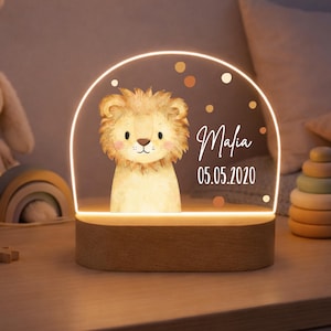 Könnte beinhalten: Nachtlicht mit Holzsockel und Löwenillustration. Der Löwe befindet sich auf einer klaren, bogenförmigen Platte mit dem Namen "Mafia" und dem Datum "05.05.2020" in Weiß. Das Licht strahlt warm, und es gibt dekorative Punkte.