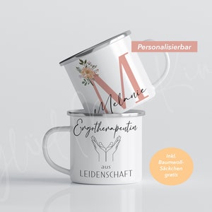 May include: Two white enamel mugs with silver lids. The top mug has a pink letter M with floral accents and the name "Melanie" written below. The bottom mug has the text "Emgotherapeutin aus LEIDENSCHAFT" and a graphic of two hands with palms facing up. The text "Ink. Baumwoll-S&auml;ckchen gratis" is in a circle on the right side of the image.