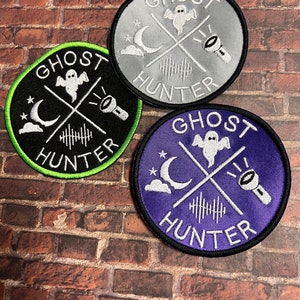 May include: Three embroidered patches with the text "Ghost Hunter" in white lettering on a black, gray, and purple background. Each patch features a white ghost, crescent moon, and flashlight.