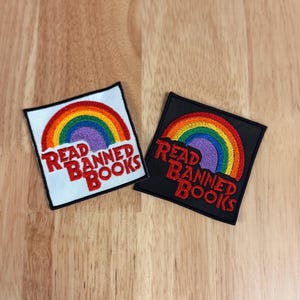 May include: Two square patches with a rainbow design and the text "Read Banned Books." One patch is on a white background, the other on black. The rainbow features red, orange, yellow, green, blue, and purple colors.