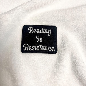 May include: Black fabric patch with white embroidery that reads "Reading is Resistance".