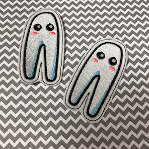 May include: Two white felt ghost appliques with black outlines and blue accents. Each ghost has two black eyes and pink cheeks.