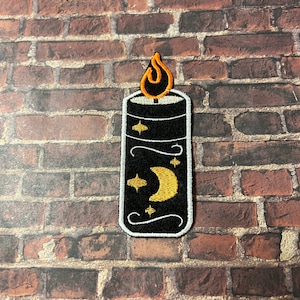 May include: Black embroidered iron-on patch of a candle with a yellow flame and a crescent moon and stars design.
