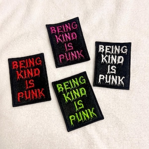 May include: Four black embroidered patches with the text "BEING KIND IS PUNK" in various colors: red, pink, green, and white. The patches are rectangular with a black border and are displayed on a white, textured surface.