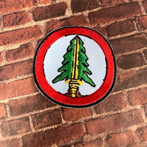May include: A red, white, and green embroidered patch with a stylized pine tree and a sword inside a circle.