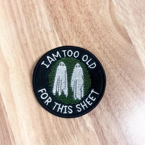 May include: A black and green embroidered patch with two white ghosts and the text "I am too old for this sheet".