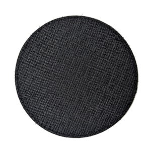 May include: A round, black patch with a textured surface. The patch is made of a woven material and has a circular shape. The background is white.