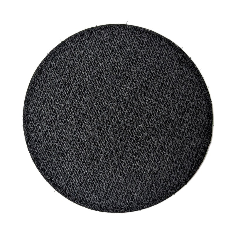 May include: A round, black patch with a textured surface. The patch is made of a woven material and has a circular shape. The background is white.