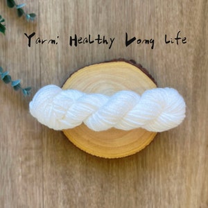 May include: White yarn on a wooden round surface. The yarn is twisted and has a slight sheen. The text "Yarn: Healthy Long Life" is written above the yarn.