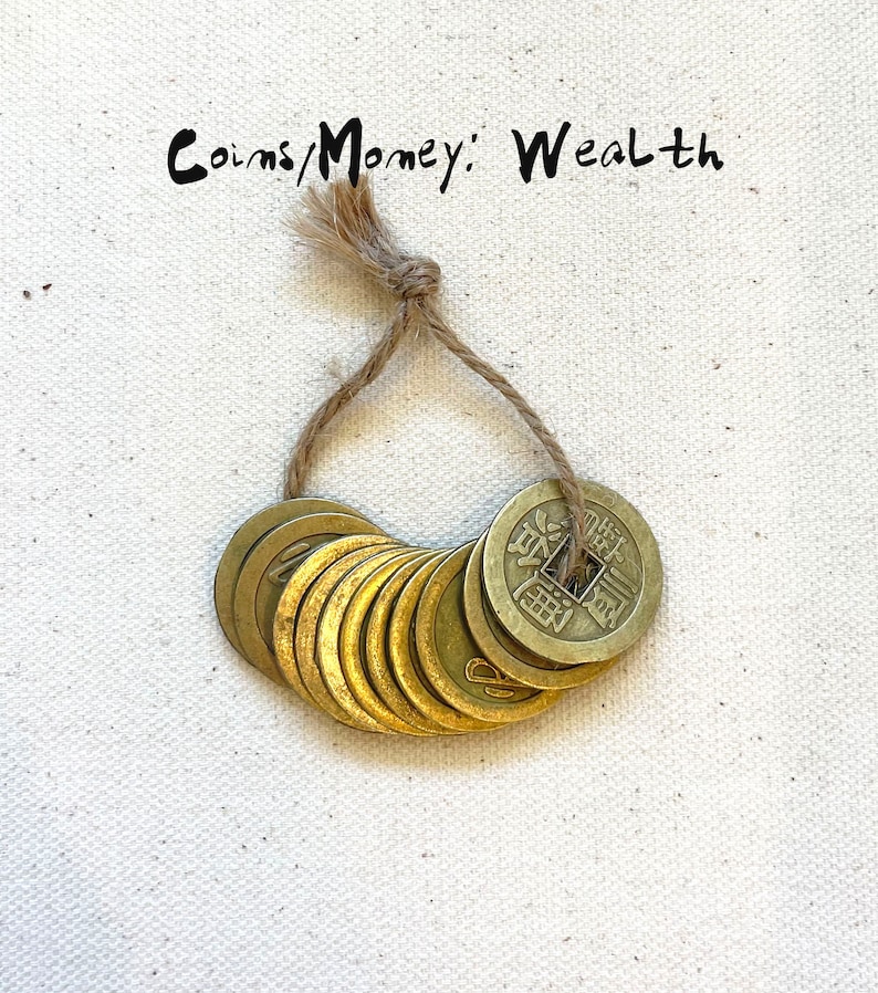 May include: A string of ten gold-colored Chinese coins tied together with twine. The coins have Chinese characters on them and are a symbol of wealth and good fortune.