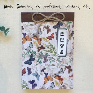 May include: A brown notebook with a butterfly pattern and a brown ribbon tied around it. The notebook has a label that says "Book: Scholars ex: professors teachers etc."