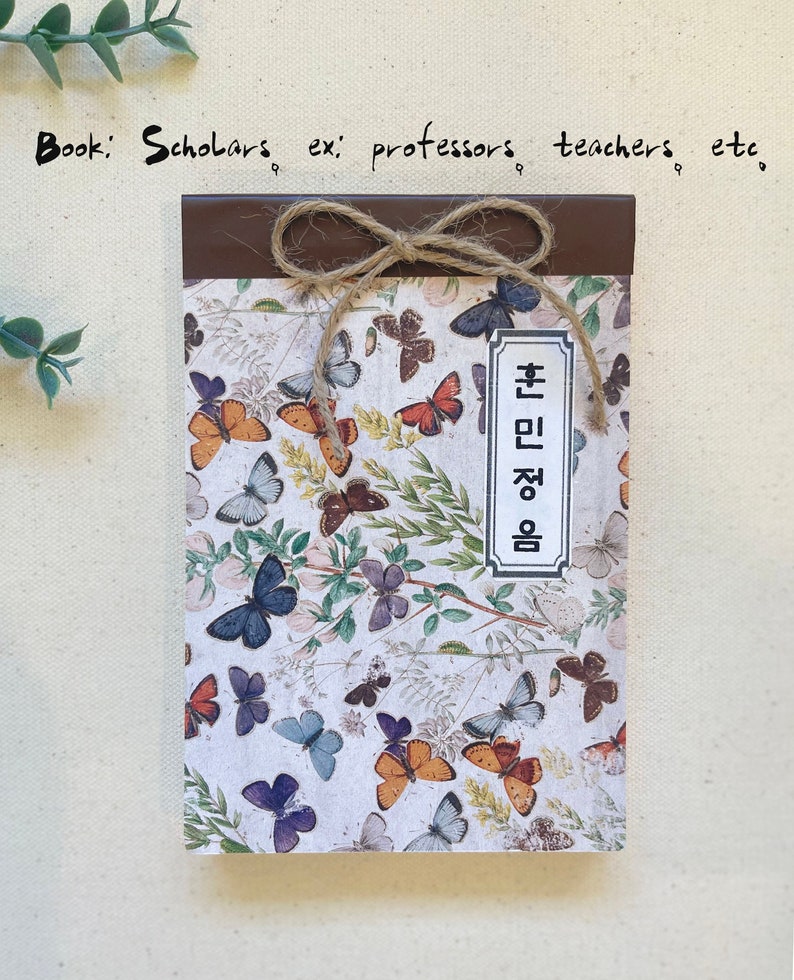 May include: A brown notebook with a butterfly pattern and a brown ribbon tied around it. The notebook has a label that says "Book: Scholars ex: professors teachers etc."