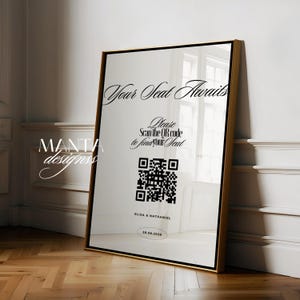 以下が含まれることがあります： 金色のフレームと白い背景の額入りサイン。「Your Seat Awaits」と書かれており、QRコードと「Please Scan the QR code to find your Seat」というテキストが含まれています。「ELIZA & NATHANIEL」という名前と「28.08.2028」という日付も表示されています。