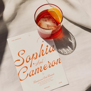 May include: A white wedding invitation with orange text announcing the wedding of Sophia and Cameron. The invitation includes the date, location, and venue: Brentwood Oak Branch, Brentwood, CA, August 2028.