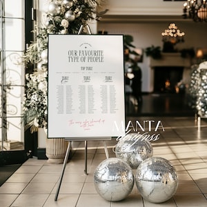 May include: A white sign with green trim on an easel displays wedding seating arrangements. The text reads "OUR FAVOURITE TYPE OF PEOPLE" and "The ones who showed up with love". Three mirrored disco balls sit in front of the sign.
