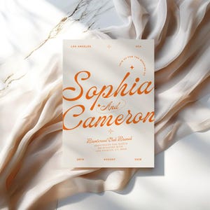 May include: A wedding invitation with a cream background and orange text. The invitation reads "Join us for the wedding of Sophia and Cameron" with a star and a circle around the text. The invitation also includes the date, August 28th, 2028, and the location, Brentwood Oak Branch, Brentwood Oak Ranch, 201 Wilshire Blvd., Los Angeles, CA 90401.
