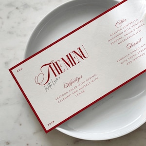 Op de afbeelding: Een rode en witte menukaart met de woorden "The Menu" in vetgedrukte rode letters. Het menu bevat voorgerechten, hoofdgerechten en desserts. De tekst "With Love x" is in cursief geschreven.