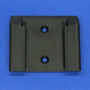 Peut inclure: Support en plastique noir de forme rectangulaire, avec deux trous circulaires et deux fentes verticales. Ce support est probablement conçu pour fixer un objet. Le fond est bleu uni.