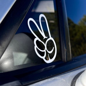 May include: A white peace sign sticker with a smiling face on a car window.