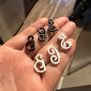 Könnte beinhalten: Ein Set aus sechs dekorativen Verzierungen, zwei schwarz und vier weiß, in Form eines stilisierten Buchstabens 'S'.