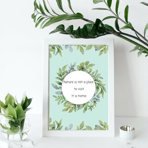 K&ouml;nnte beinhalten: Ein gerahmter Druck mit hellblauem Hintergrund und einer Aquarell-Illustration von gr&uuml;nen Bl&auml;ttern. Der Druck zeigt den Text "Nature is not a place to visit. It is home."