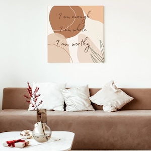 May include: A brown couch with white pillows in a living room setting. A framed print with abstract shapes and the text "I am enough, I am whole, I am worthy" hangs on the wall above the couch.