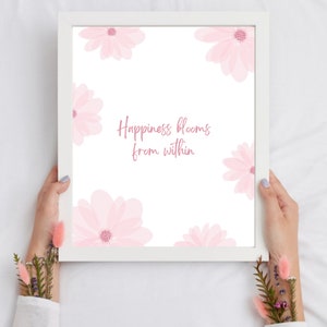 K&ouml;nnte beinhalten: Ein wei&szlig;er gerahmter Druck mit einem rosafarbenen Blumendesign und dem Text "Happiness blooms from within".