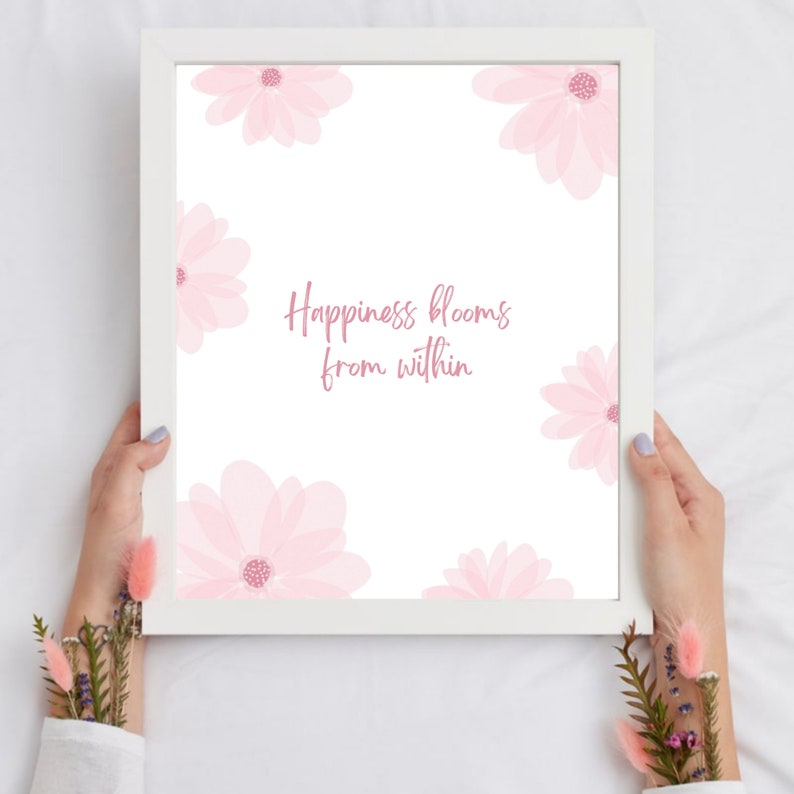 K&ouml;nnte beinhalten: Ein wei&szlig;er gerahmter Druck mit einem rosafarbenen Blumendesign und dem Text "Happiness blooms from within".