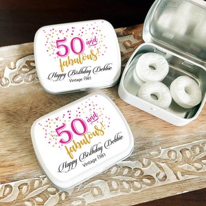 May include: Two white metal tins with pink and gold confetti designs. The tins have the text "50 and fabulous!" and "Happy Birthday Debbie Vintage 1981". The tin on the right is open and contains three white mints.