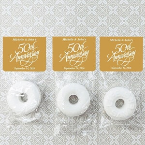 May include: Three white favor mints wrapped in clear cellophane bags with gold square labels that read "Michelle & John's 50th Anniversary September 14, 2026".