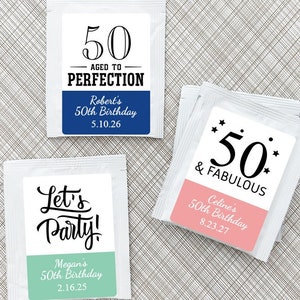 May include: Three white tea bags with colorful labels. The labels have black text that says "50 Aged to Perfection", "Let's Party!" and "50 & Fabulous". Each label has a different colored background and includes a name and date.