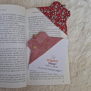 Puede incluir: Dos marcapáginas de tela origami en un libro. Uno es rojo con estampados florales blancos, el otro es rosa con detalles dorados. También es visible una tarjeta blanca con el texto "origami tissu" y "Je suis un marque-page!"
