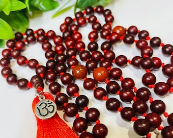 May include: A red wooden mala bead necklace with a silver Om charm and a red tassel. The beads are strung on a red cord.
