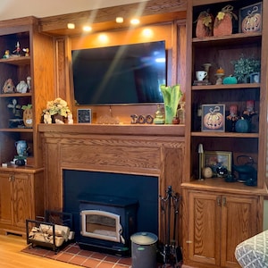 May include: A wood-paneled entertainment center with a fireplace, a television, and shelves decorated with Halloween-themed items. The shelves are filled with various decorative items, including pumpkins, gourds, and candles.