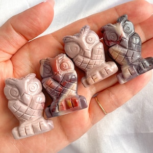 May include: Four carved owl figurines made of pink, red, and grey stone. The owls are all facing forward and have their wings spread out.