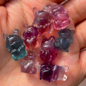 May include: A collection of small, colorful, translucent figurines shaped like animals. The figurines are made of glass or resin and have a variety of colors, including purple, pink, blue, and green.