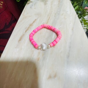 May include: Pink and white stretchy bracelet with a silver seashell charm.