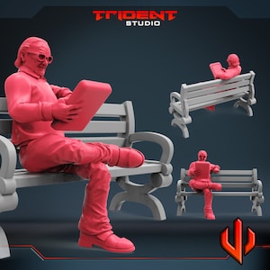 May include: A pink figurine of a person sitting on a gray bench, holding a tablet. The person is wearing a jacket and pants. The bench has a slatted back and seat.