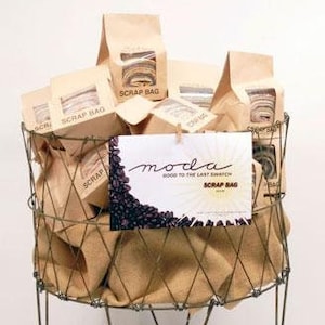 May include: A wire laundry basket with wheels, filled with brown paper bags labeled "Scrap Bag" and a sign that reads "moda good to the last stitch Scrap Bag".