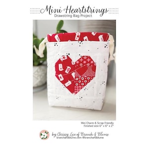 May include: A white quilted drawstring bag with a red heart applique. The heart is made of various red fabrics with white accents. The bag has a red interior and is labeled "Mini Heartstrings Drawstring Bag Project". Finished size is 6" x 6" x 2".