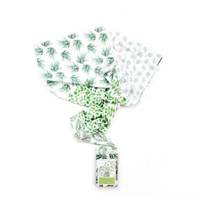 May include: A white muslin swaddle blanket with a green leafy pattern. The blanket is folded and tied in a knot. The packaging label reads "The Little Green Collection".