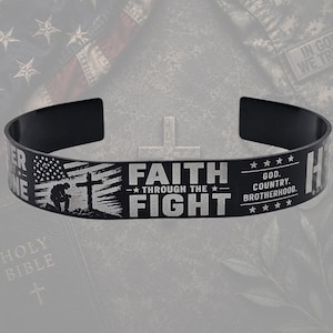 May include: A black cuff bracelet featuring engraved silver-toned text that reads FAITH THROUGH THE FIGHT, GOD. COUNTRY. BROTHERHOOD. The design includes a graphic of a kneeling soldier before a cross and a stylized American flag motif.