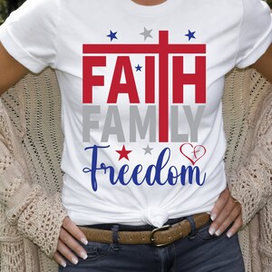 May include: White t-shirt with a red, white, and blue graphic that says "FAITH FAMILY FREEDOM" with a cross and stars.
