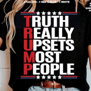 以下が含まれることがあります： 白い文字で「TRUTH REALLY UPSETS MOST PEOPLE」と書かれた黒いTシャツ。テキストは縦に配置され、「TRUMP」の文字が縦の列を形成しています。テキストは赤と青のストライプと星で囲まれています。